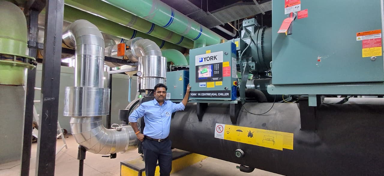 GS Aircon engineer beside a YORK YK centrifugal chiller with insulated chilled-water headers overhead